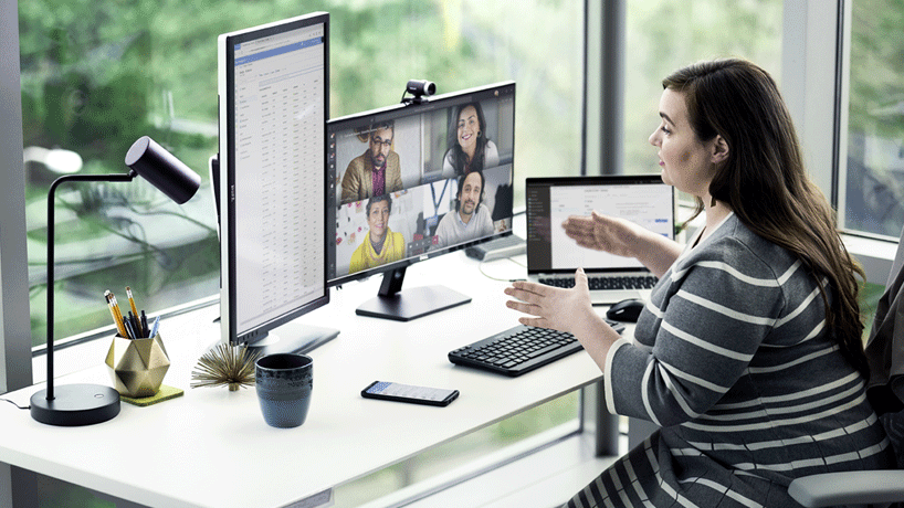 A woman seated at a window with multiple devices using Teams to get help with app submissions.