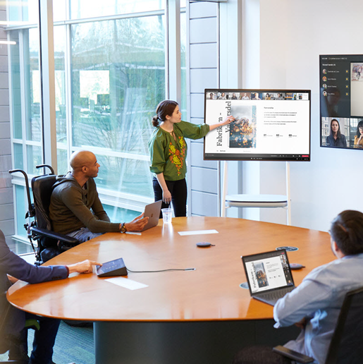 A woman presenting using PowerPoint to group of people in a conference room and on Teams